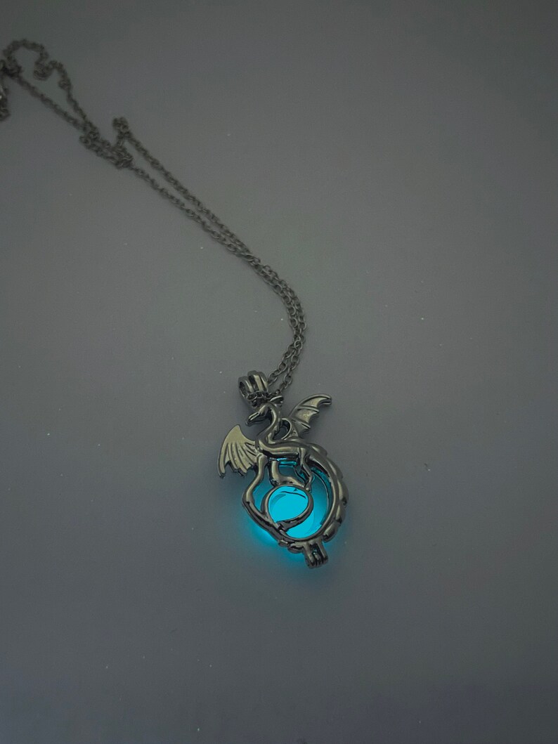 May include: A silver necklace with a dragon pendant. The dragon is curled around a glowing blue orb.