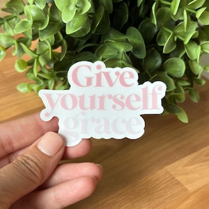 May include: Pink and white sticker with the text "Give yourself grace" in a bold, stylized font.