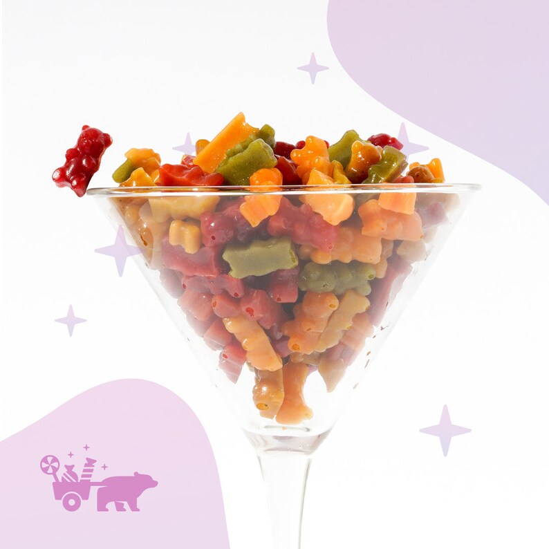 May include: A glass martini glass filled with colourful gummy bears. The gummy bears are in various shapes and colours, including red, orange, yellow, green, and purple.
