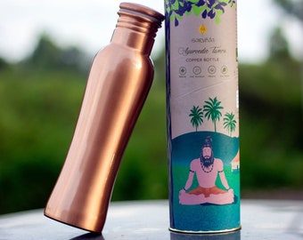 May include: A copper water bottle with a curved shape and a brown label that says "Sarveda Ayurvedic Tamra Copper Bottle". The label has a green background with illustrations of palm trees and a man meditating.