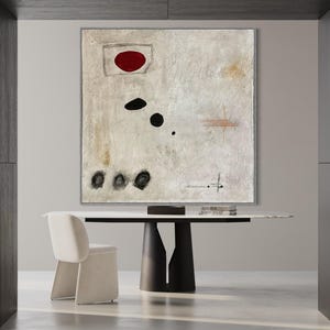 May include: Abstract painting with a red circle, black dots, and lines on a white background. The painting is framed and hanging on a wall above a table with a white top and black legs.