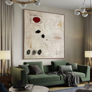 May include: A green sofa with black and white patterned pillows and a black and white throw blanket. A large abstract painting with a red circle and black shapes hangs above the sofa. The painting is on a white wall.