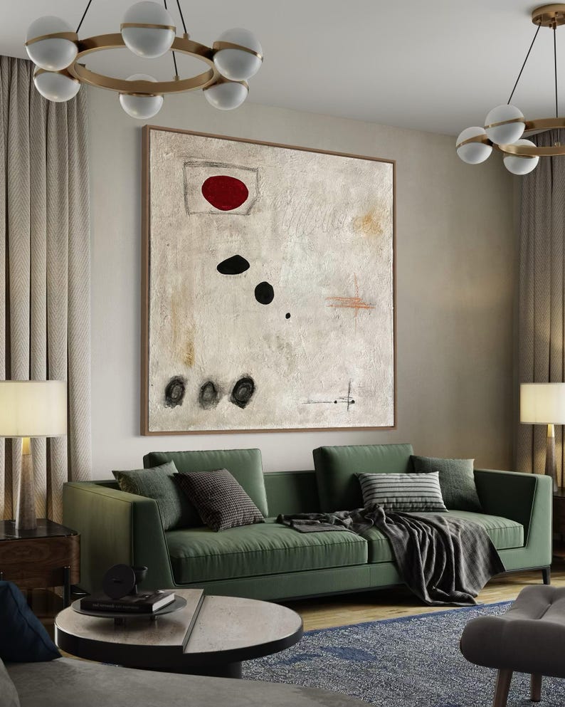 May include: A green sofa with black and white patterned pillows and a black and white throw blanket. A large abstract painting with a red circle and black shapes hangs above the sofa. The painting is on a white wall.