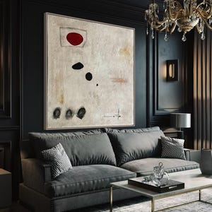 May include: A dark gray sofa with a black and white patterned throw pillow in a living room with a large abstract painting featuring a red circle and black shapes. The painting is on a black wall with gold trim. The room has a black coffee table with a glass tray and a vase with flowers.