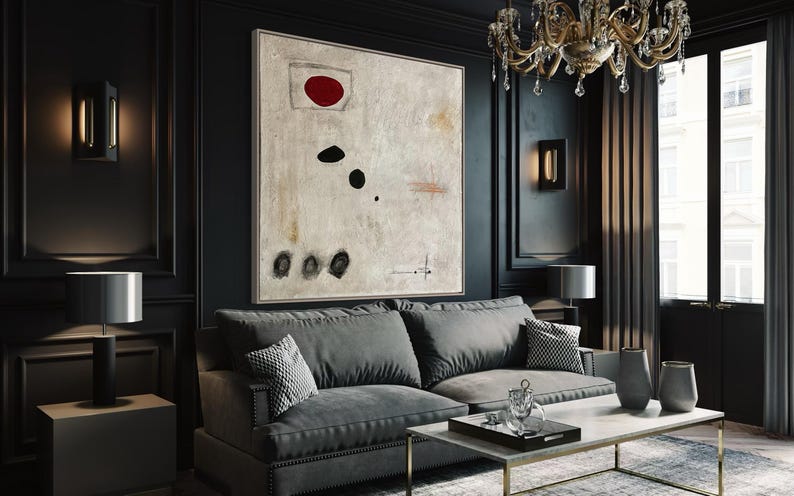 May include: A dark gray sofa with a black and white patterned throw pillow in a living room with a large abstract painting featuring a red circle and black shapes. The painting is on a black wall with gold trim. The room has a black coffee table with a glass tray and a vase with flowers.