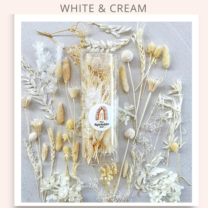 May include: A clear glass jar filled with dried white and cream colored flowers. The jar is labeled "The Sprinkle Bar".
