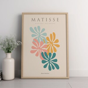 May include: A framed print with a minimalist design featuring colorful cut-out shapes in shades of teal, pink, and yellow. The print is titled "Matisse, Papiers Decoupes" and is signed "Henri Matisse".