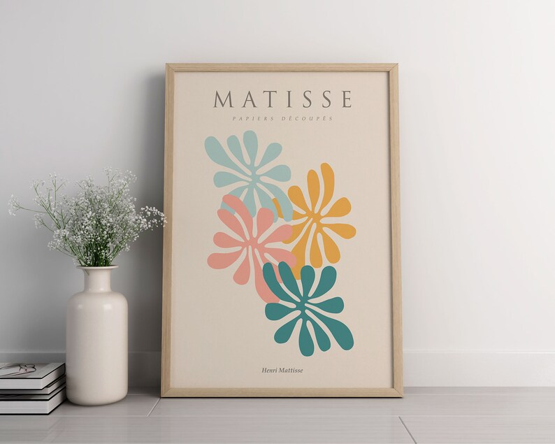 May include: A framed print with a minimalist design featuring colorful cut-out shapes in shades of teal, pink, and yellow. The print is titled "Matisse, Papiers Decoupes" and is signed "Henri Matisse".