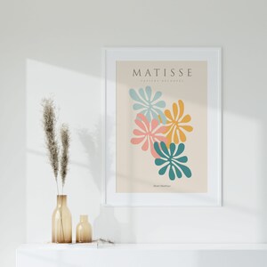 May include: A white framed print with the text "MATISSE PAPIERS DECOUPES" and the artist's name "Henri Matisse" in a light brown font. The print features a colorful abstract design of overlapping teal, pink, yellow, and blue shapes.