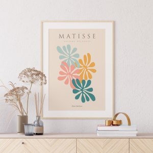 May include: A framed print of a Matisse artwork featuring colorful cut-out paper flowers in shades of teal, pink, and yellow. The title "MATISSE PAPIERS DECOUPES" and the artist's name "Henri Matisse" are printed below the artwork.