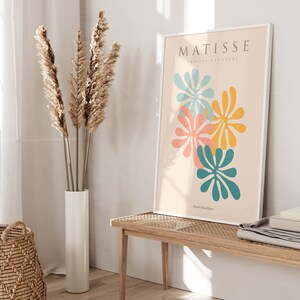 May include: A white framed print with the text "MATISSE papiers d&eacute;coup&eacute;s" and the artist's name "Henri Matisse" at the bottom. The print features four abstract flower shapes in shades of blue, yellow, pink, and orange on a cream background.