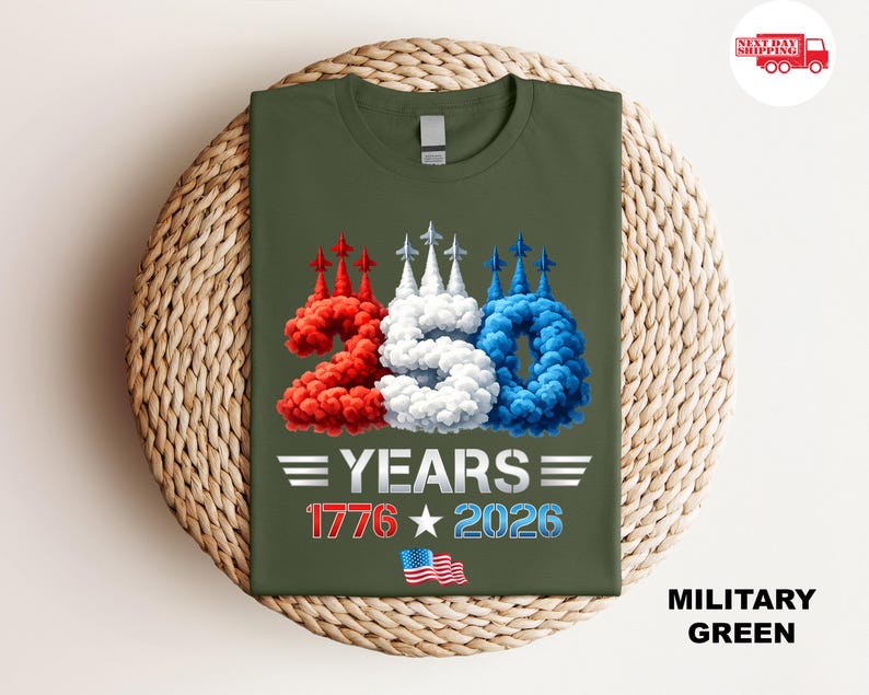 Puede incluir: Camiseta verde militar con un dise&ntilde;o gr&aacute;fico que celebra 250 a&ntilde;os. El dise&ntilde;o incluye el n&uacute;mero "250" en humo rojo, blanco y azul, el texto "YEARS", las fechas "1776" y "2026", y una bandera estadounidense.