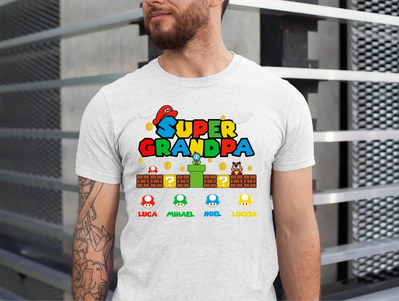 Op de afbeelding: Wit T-shirt met een Super Opa-afbeelding in Mario-stijl. De afbeelding bevat een groene pijp, munten en vier paddenstoelfiguren met de namen Luca, Michael, Noel en Lucia.