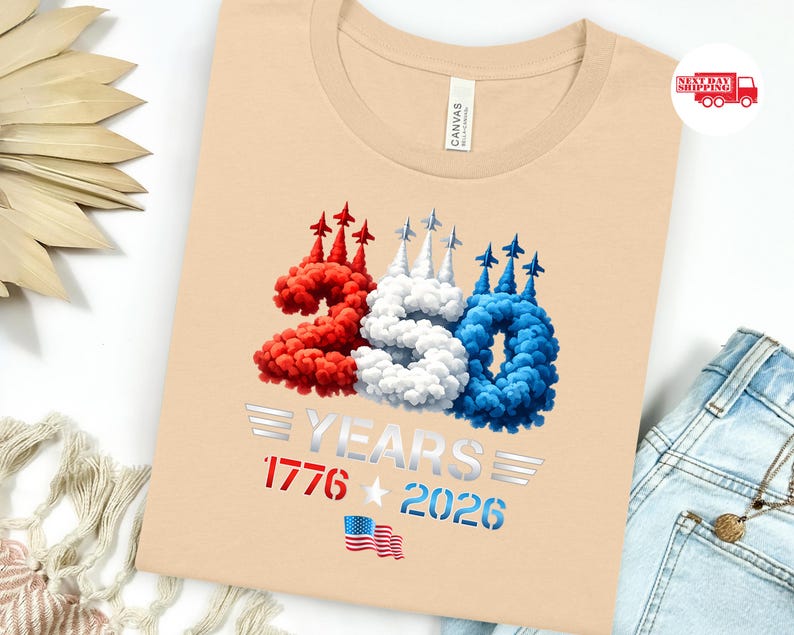 Puede incluir: Una camiseta beige con un dise&ntilde;o patri&oacute;tico que celebra 250 a&ntilde;os. El n&uacute;mero "250" est&aacute; en rojo, blanco y azul, imitando estelas de humo con peque&ntilde;os aviones. El texto "YEARS 1776 2026" est&aacute; debajo, junto con una peque&ntilde;a bandera estadounidense.