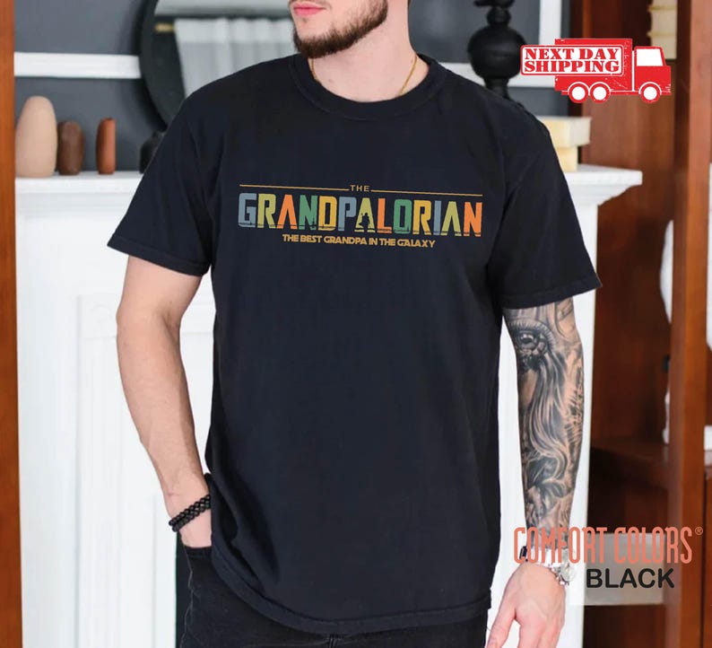 May include: Black t-shirt with a colorful graphic that says "The Grandpalorian The Best Grandpa in the Galaxy".