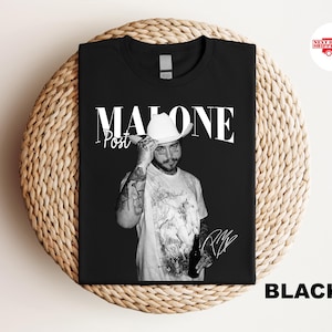 May include: Black t-shirt featuring a black and white image of Post Malone. The image shows Post Malone wearing a white cowboy hat and holding a bottle. The word "MALONE" is printed above the image, with "Post" below.