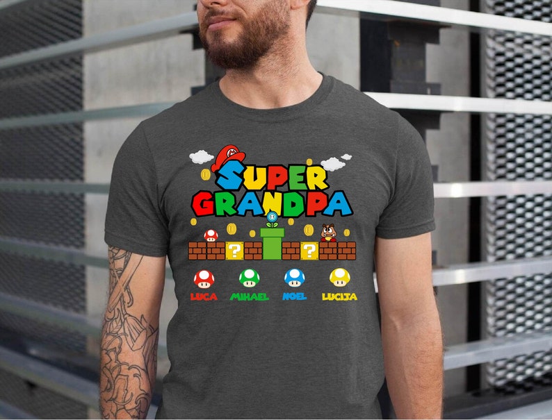 Op de afbeelding: Een donker grijs gem&ecirc;leerd t-shirt met een Super Mario Bros.-thema. De afbeelding bevat de tekst "Super Grandpa" met een paddenstoel, pijp en vraagtekenblok. De namen Luca, Mikael, Noel en Lucia staan onder de afbeelding.