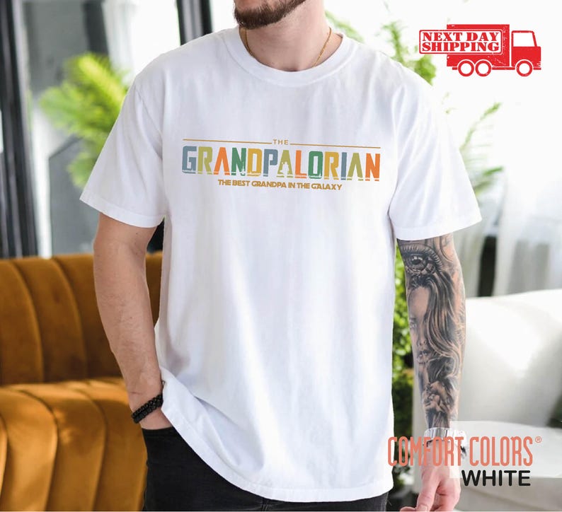 May include: White t-shirt with the text "The Grandpalorian The Best Grandpa in the Galaxy" in colorful letters.