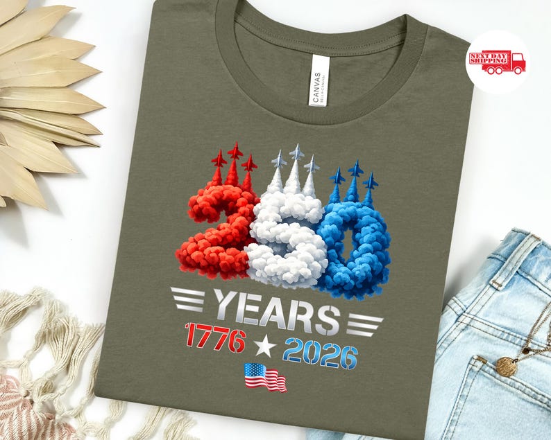 Puede incluir: Camiseta verde oliva con un dise&ntilde;o patri&oacute;tico. El dise&ntilde;o presenta el n&uacute;mero 250 en rojo, blanco y azul, con el texto "YEARS 1776 2026" y una bandera americana. La camiseta est&aacute; hecha de un material suave.