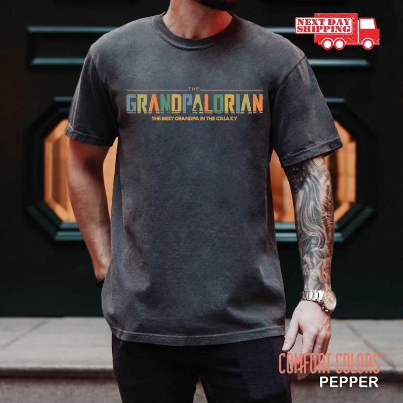May include: A dark gray t-shirt with a vintage-style graphic that reads "The Grandpalorian, The Best Grandpa in the Galaxy".