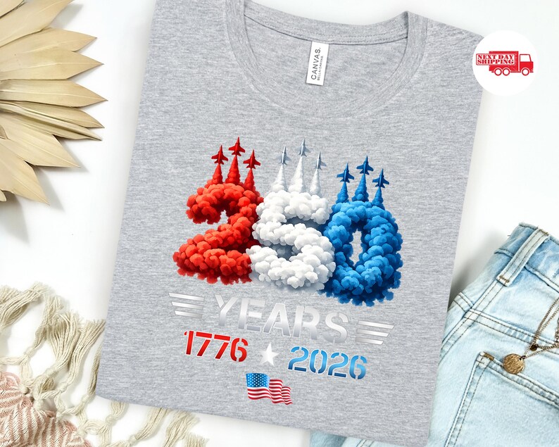 Puede incluir: Una camiseta gris con un dise&ntilde;o patri&oacute;tico. El dise&ntilde;o presenta los n&uacute;meros "250" en rojo, blanco y azul, con el texto "YEARS 1776 2026" y una bandera estadounidense. La camiseta est&aacute; hecha de un material suave.