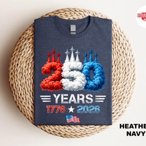 Puede incluir: Camiseta azul marino con un dise&ntilde;o patri&oacute;tico. El gr&aacute;fico presenta el n&uacute;mero "250" en rojo, blanco y azul, con el texto "YEARS 1776 2026" y una peque&ntilde;a bandera estadounidense. La camiseta se muestra sobre una superficie tejida.
