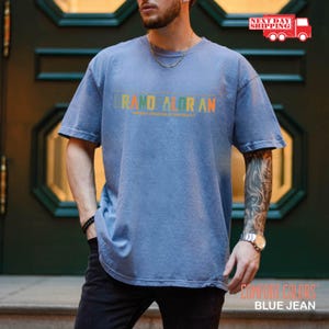 May include: A blue jean t-shirt with the text "GRAND ALORAN" in a rainbow color gradient. The text is centered on the shirt and is slightly faded.