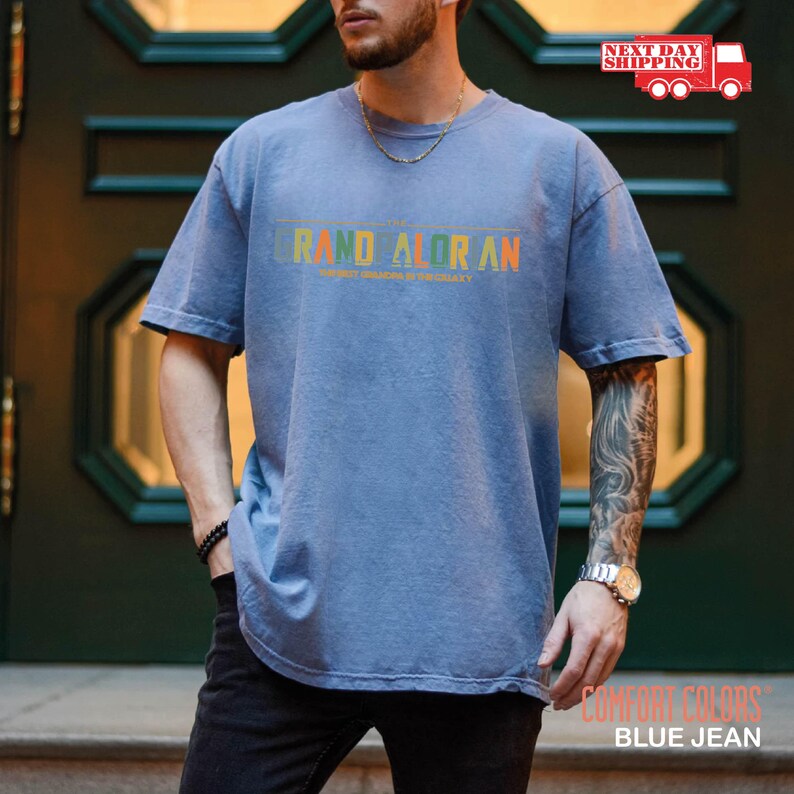 May include: A blue jean t-shirt with the text "GRAND ALORAN" in a rainbow color gradient. The text is centered on the shirt and is slightly faded.
