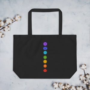 Pode incluir: Sacola tote preta com uma linha vertical de sete s&iacute;mbolos de chakras coloridos. Os s&iacute;mbolos est&atilde;o dispostos na ordem dos chakras, come&ccedil;ando com o chakra raiz na parte inferior e terminando com o chakra coroa na parte superior.