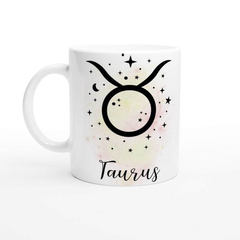 May include: White ceramic mug with a black Taurus zodiac symbol and a watercolor background of stars and a crescent moon. The word "Taurus" is written in black cursive at the bottom of the mug.