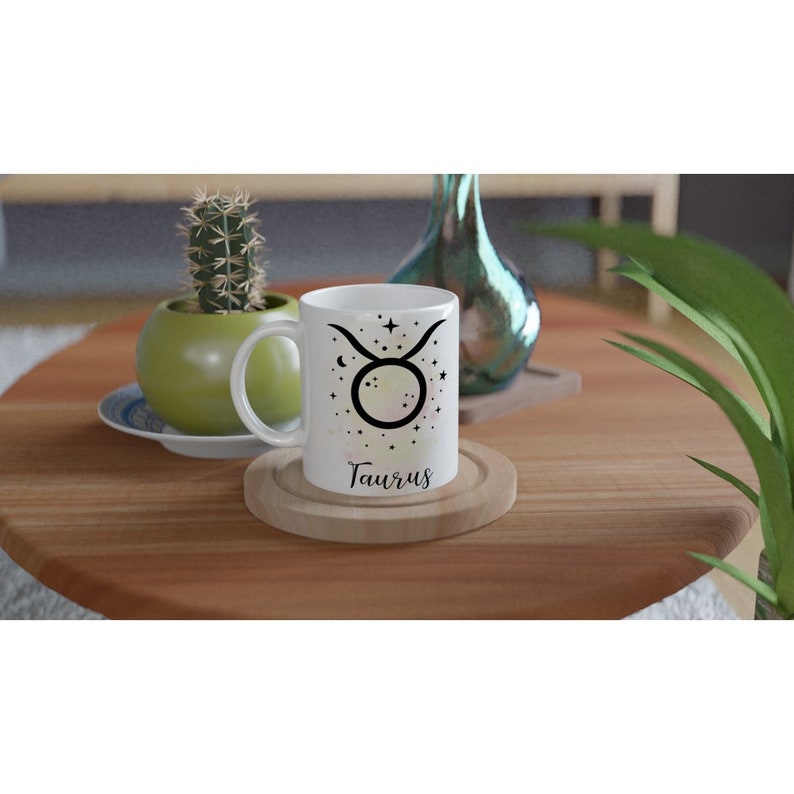 May include: White ceramic mug with a black Taurus zodiac symbol and stars. The mug has the word "Taurus" written in black cursive below the symbol.