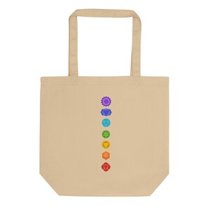 Puede incluir: Una bolsa de tela beige con una fila vertical de siete s&iacute;mbolos de chakras coloridos impresos en la parte delantera.