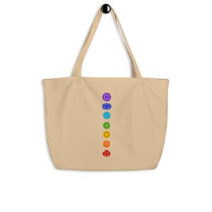 Pode incluir: Uma bolsa tote bege com uma linha vertical de sete s&iacute;mbolos de chakras coloridos impressos na frente.