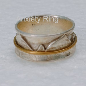 Peut inclure: Une bague d'anxiété en argent et or avec une bande tournante. La bague a un design texturé.