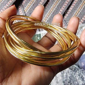 May include: A stack of gold-colored metal bangles. The bangles are stacked on top of each other and are all the same size.