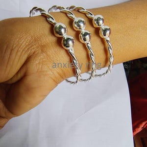 May include: Three silver bangle bracelets with twisted rope designs and three silver beads on each bracelet.