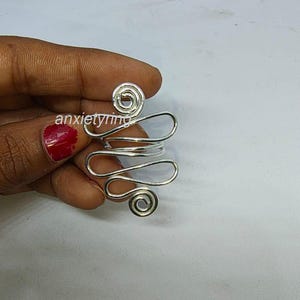 Könnte beinhalten: Ein silberner Drahtring mit einem einzigartigen Design mit mehreren Schleifen und Spiralen. Der Ring ist aus dünnem Draht gefertigt und hat eine zarte, luftige Optik.
