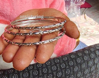 May include: Three silver bangles with a textured design. The bangles are stacked on top of each other.
