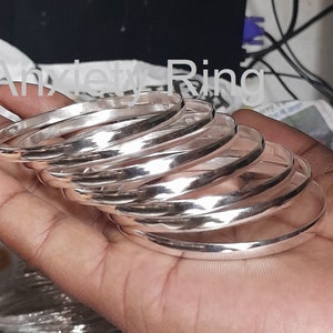 May include: A stack of silver bangles, stacked on top of each other, in a person's hand. The bangles are smooth and shiny.