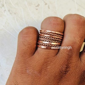 May include: A set of seven copper rings stacked on a finger. The rings are of varying widths and have a hammered and twisted texture.