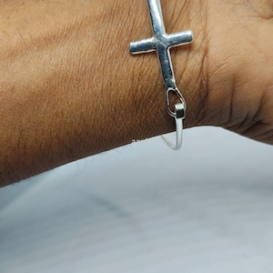 May include: A silver cross charm bracelet. The bracelet is made of a thin silver chain with a large cross charm in the center.