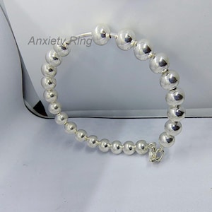 Puede incluir: Un brazalete de plata con cuentas redondas. El brazalete tiene un cierre de broche y un diseño simple.