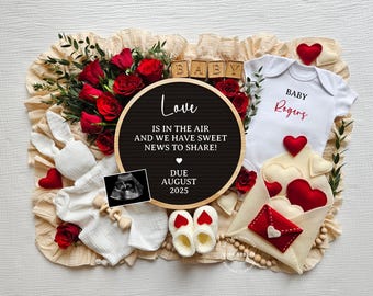 May include: A pregnancy announcement featuring a black chalkboard sign that reads "Love is in the air and we have sweet news to share! Due August 2025". The sign is surrounded by red roses, a white babygrow with "Baby Rogers" in red lettering, a white bunny rattle, and a white envelope with red hearts.