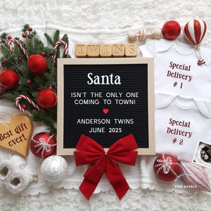 May include: A festive announcement featuring a black felt letter board with the text "Santa isn't the only one coming to town!" and "Anderson Twins June 2025." Includes baby onesies, Christmas ornaments, and a wooden heart.
