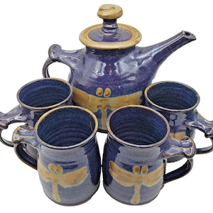 Könnte beinhalten: Ein Keramik-Teeservice mit einer Teekanne und vier Tassen. Das Set ist überwiegend blau mit goldenen Akzenten und Libellenmustern. Die Teekanne hat einen Deckel und einen Ausguss. Die Tassen haben Henkel.