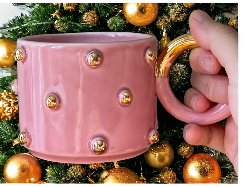 May include: A pink ceramic mug with a gold handle and gold dots around the mug.
