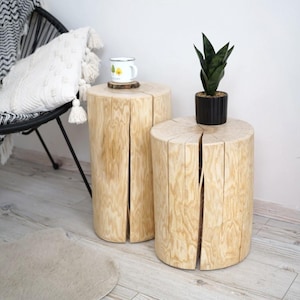 Op de afbeelding: Twee houten stompe bijzettafels met een natuurlijke houten afwerking. De tafel links heeft een witte keramische mok erop. De tafel rechts heeft een groene plant in een pot erop.