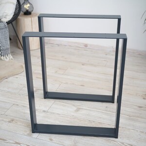 Könnte beinhalten: Zwei dunkelgraue Tischbeine aus Metall mit quadratischem Rahmen. Die Beine sind aus robustem Metall gefertigt und haben ein schlichtes, modernes Design.