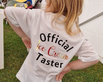 May include: A white t-shirt with the text "Official Ice Cream Taster" printed on the back. The text is in black with gold and red accents.