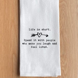 May include: White kitchen towel with the text "Life is short. Spend it with people who make you laugh and feel loved." The design includes an arrow and heart symbol.